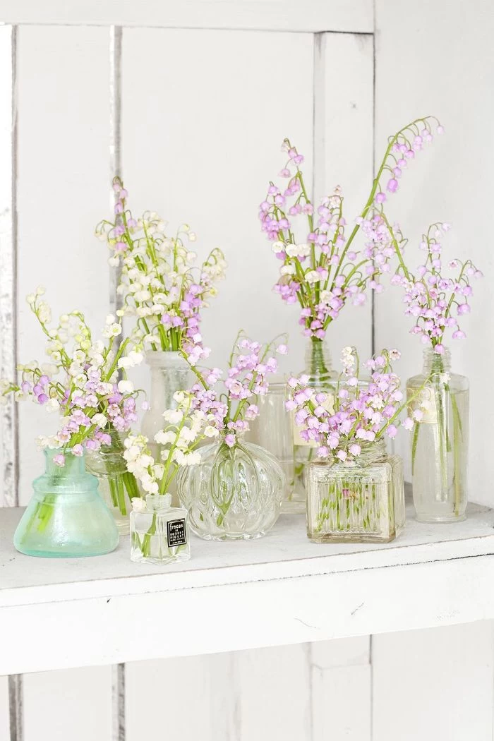 glass vases in different shapes placed on wooden shelf outdoor easter decorations white and purple flowers in them