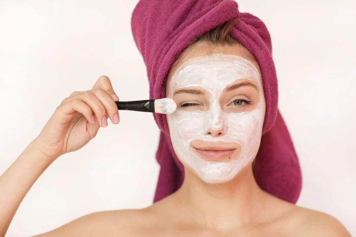 homemade face mask for acne woman wearing purple head towel putting mask on her face with brush