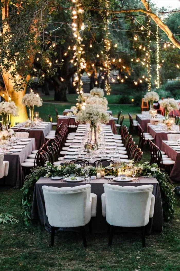 long table with large flower bouquets in the middle backyard wedding decorations strings of lights hanging from trees