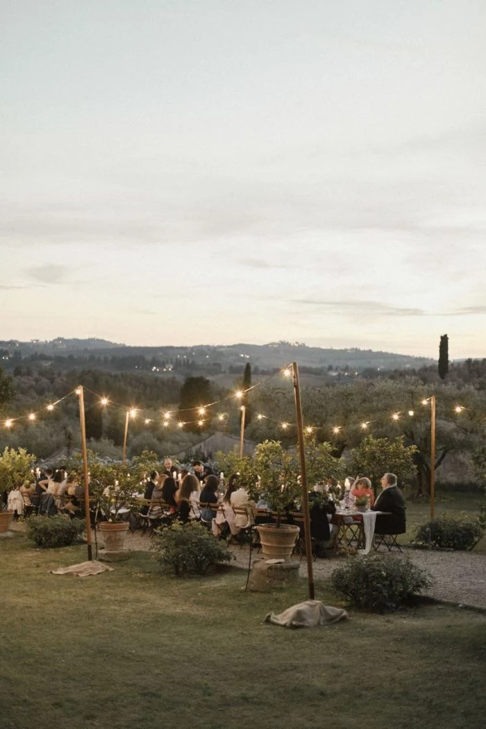 long table with lots of people sitting around it outdoor wedding decorations strings of lights on both sides