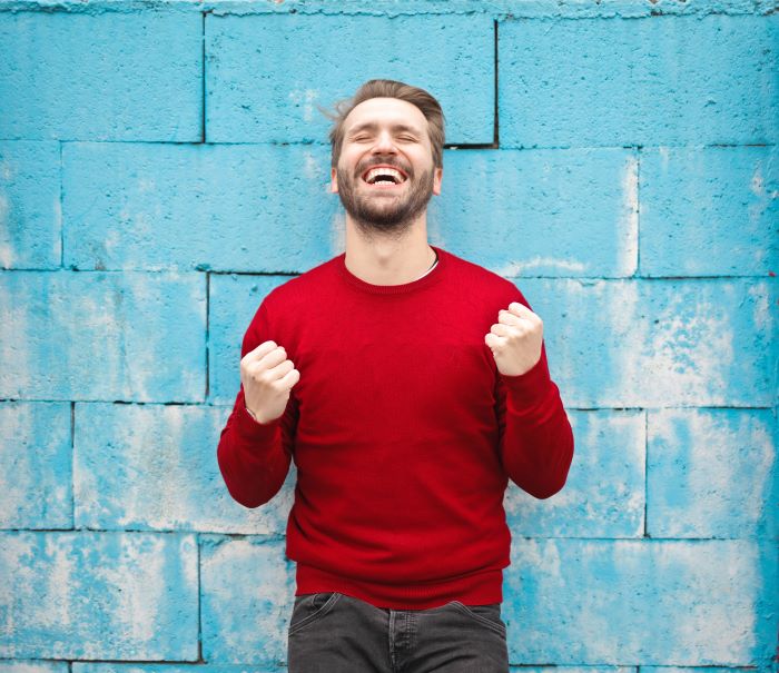 man wearing red sweater black jeans smiling food education standing in front of blue wall