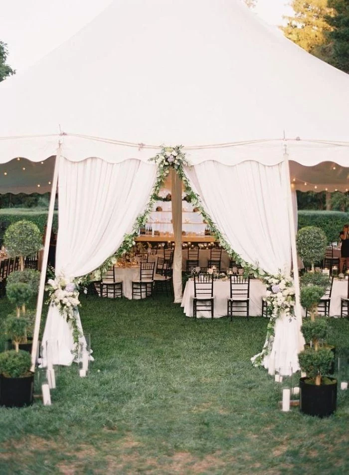 outdoor wedding decorations entrance arch with white curtains and flowers leading to tent with tables under it