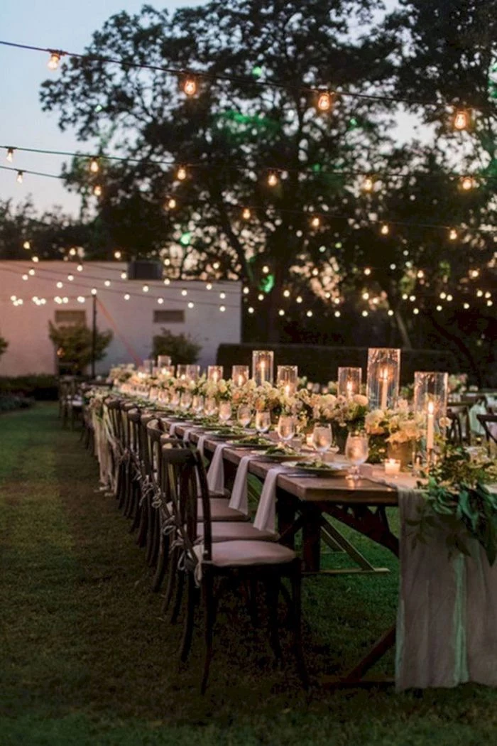 outside wedding ideas long table with a floral table runner with candles lots of chairs around it