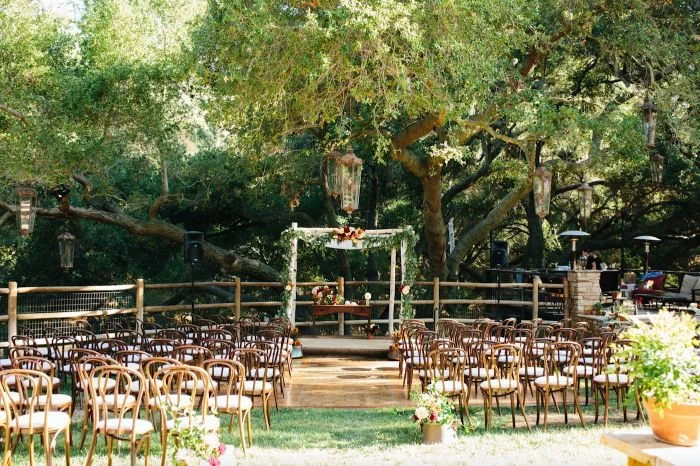 rustic wedding ideas arch with flowers table underneath lots of chairs placed under large tree