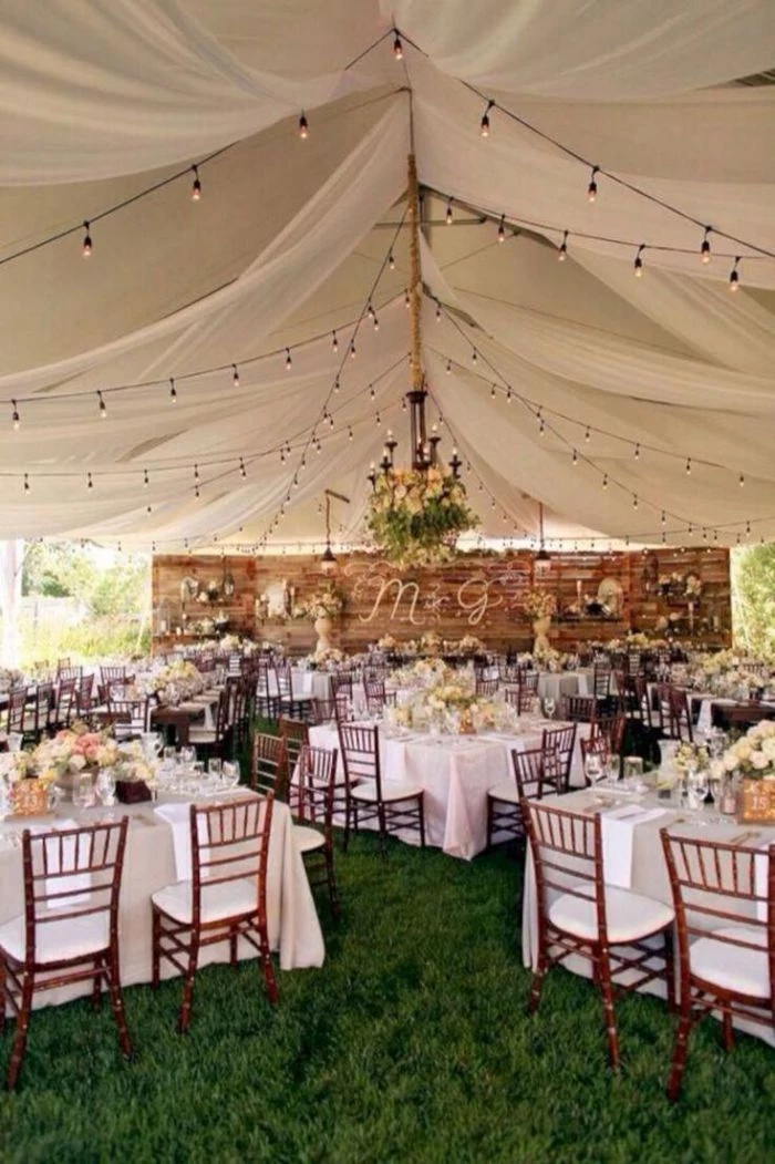 tent with white curtains string of lights backyard wedding ideas lots of tables with wood chairs flower bouquets