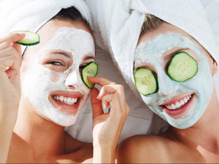 two women wearing white face masks honey face mask two cucumber slices on their eyes