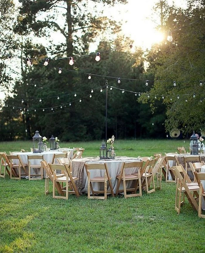 white table cloths on round tables arranged under strings of lights backyard wedding reception minimalistic decor