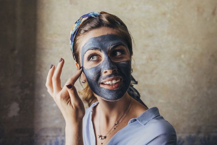 woman putting dark face mask on her face hydrating face mask wearing blue shirt