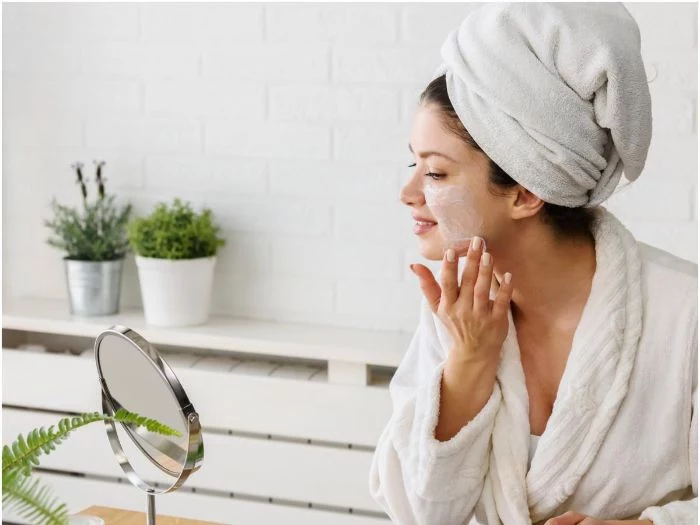 woman putting mask on her face homemade face mask for acne wearing white bath robe towel on her head