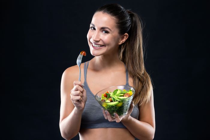 woman smiling holding a bowl full of salad food education holding fork with halved cherry tomato