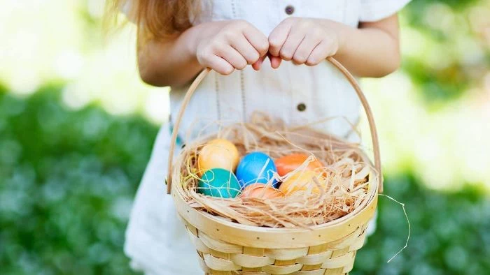 woman wearing white dress holding a basket adult easter basket filled with dyed easter eggs