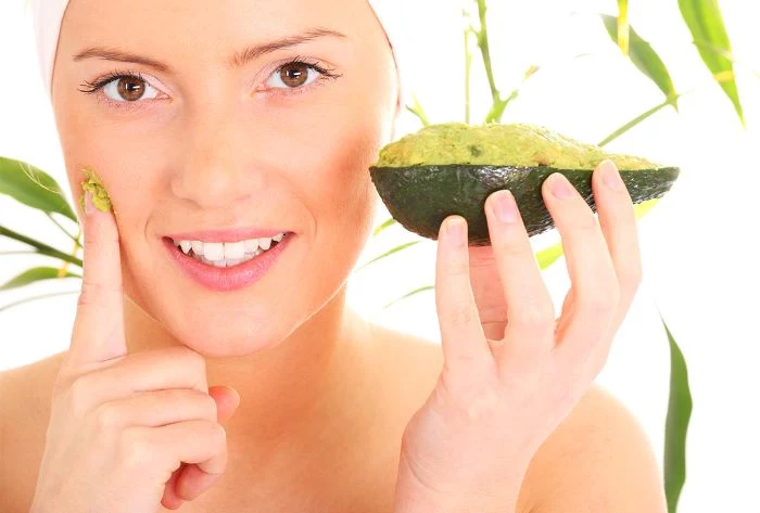 woman wearing white towel on her head diy face masks putting avocado mask on her face