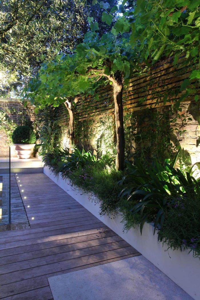 backyard string lights wooden pathway flower bed next to it with lights under the trees and bushes