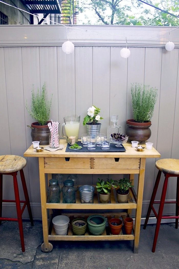 bar stools next to small cart with two shelves filled with potted plants outdoor patio bar mimosa ingredients glasses on top