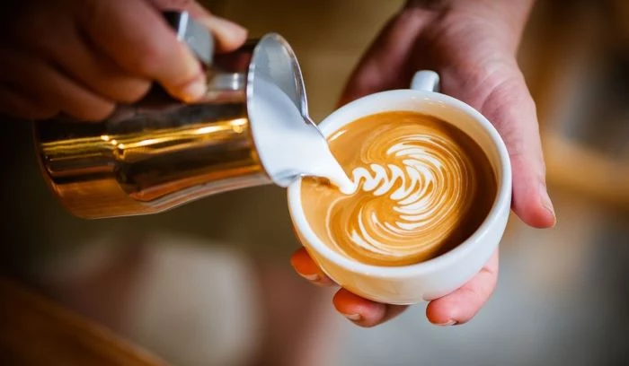barista pouring milk foam into coffee cup creating decoration how to make coffee