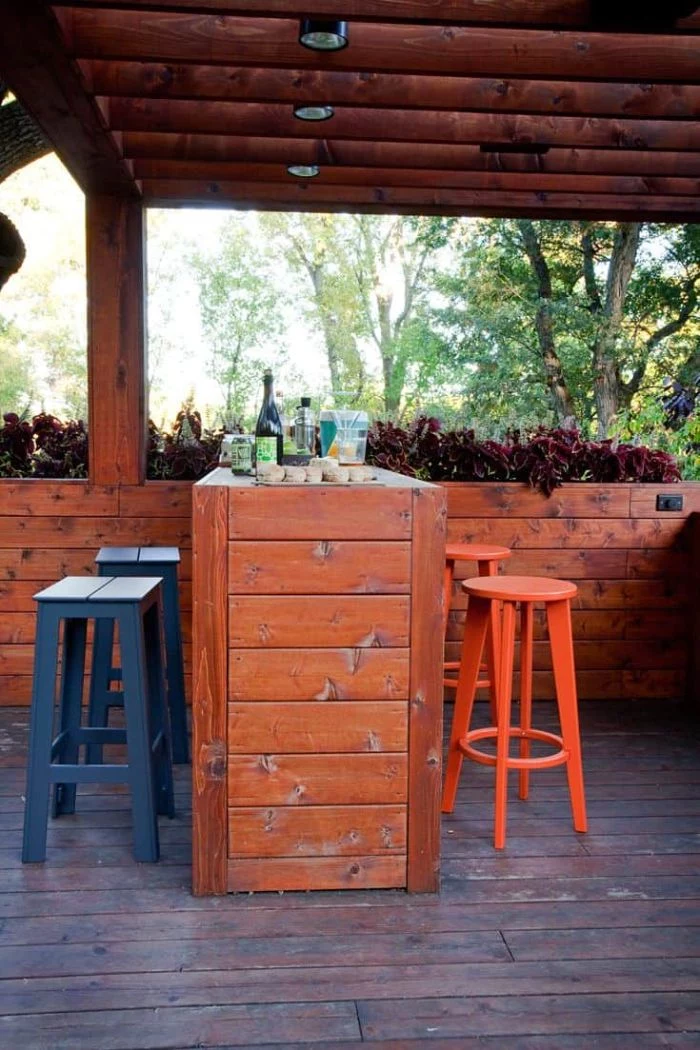 black and orange bar stools next to outdoor wooden bar inside wooden enclosure