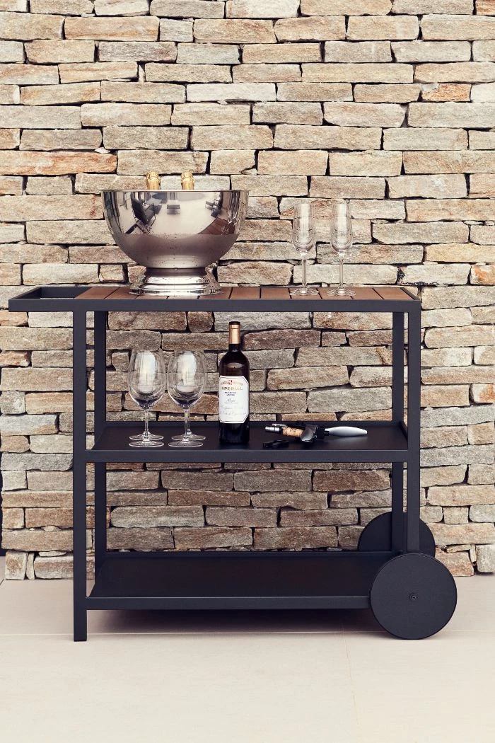 black cart with wine glasses wine bottles on the shelves outside bar ideas in front of stone wall