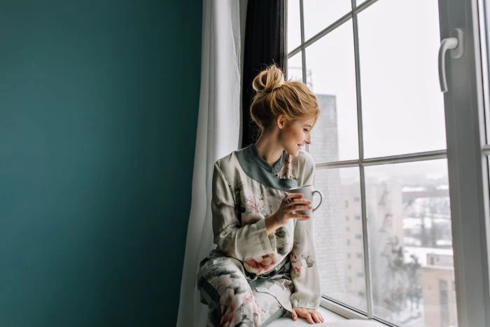 blonde woman sitting on window frame window installation drinking coffee turquoise wall