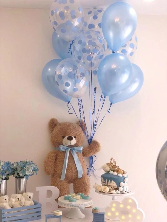 blue balloons held by teddy bear baby shower ideas for girls placed on dessert table with cake blue and white flower bouquets