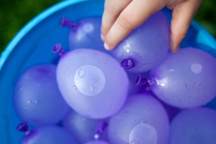 blue bucket filled with purple balloons filled with water backyard games for kids