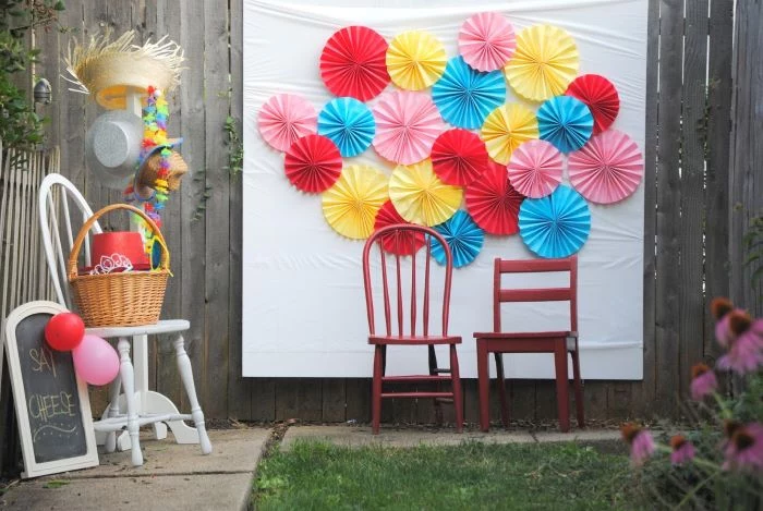 blue red pink yellow paper fans arranged on white surface baby shower decoration ideas for boy two chairs in front of it photo backdrop