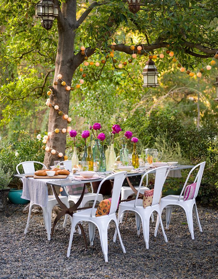 bouquets of flowers in the middle of dining table placed under a tree backyard string lights string of small lanterns wrapped around the tree