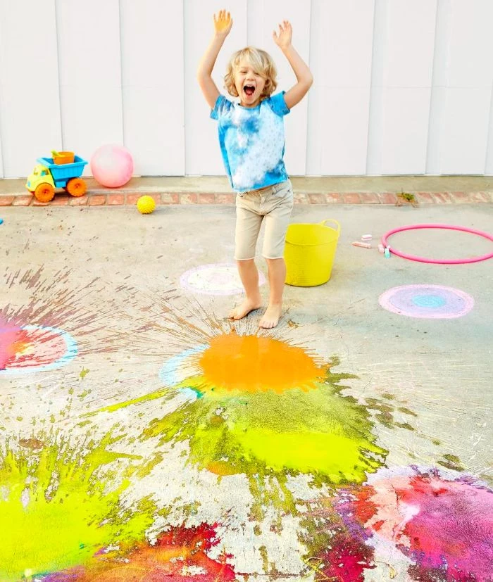boy smiling playing with paint outdoor games for kids yellow and pink paint splattered on the concrete
