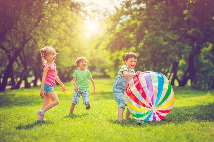 boys and girl playing on a field surrounded by trees outdoor fun for kids playing with large plastic ball