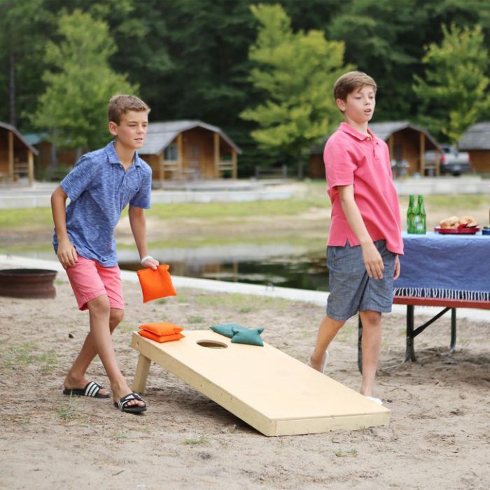 boys playing cornhole carrying corn bags backyard games for kids playing next to lake