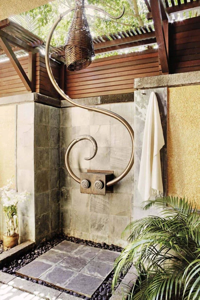 brass and rattan shower head wood outdoor shower stone tiles on the walls and floor surrounded by small rocks