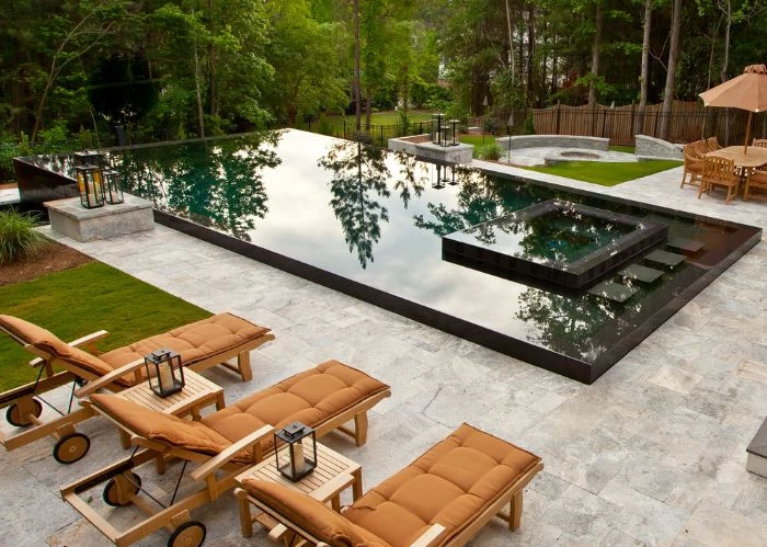 brown cushions on lounge chairs next to large pool backyard swimming pool surrounded by tall trees