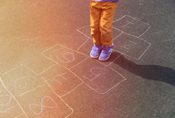 close up photo of kid wearing orange pants blue sneakers playing hop scotch outdoor activities for toddlers