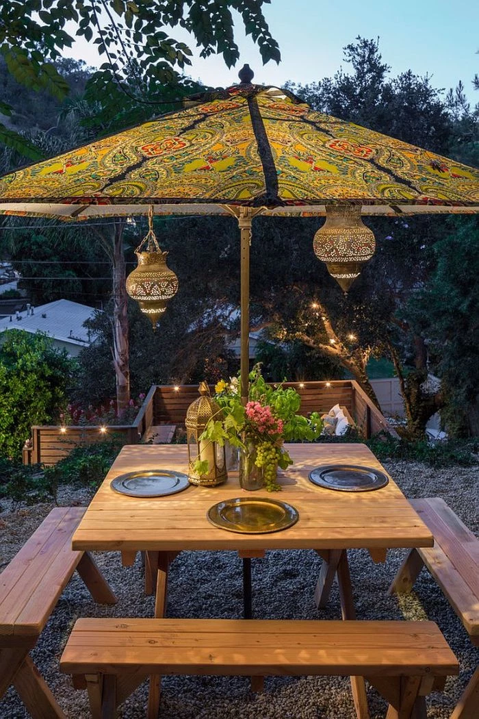 colorful umbrella placed above wooden table with benches landscape lighting ideas lanterns hanging from it