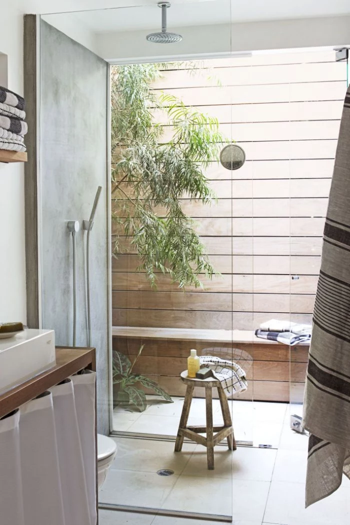 freestanding outdoor shower wood wall and bench shower next to it with tiled floor behind glass enclosure