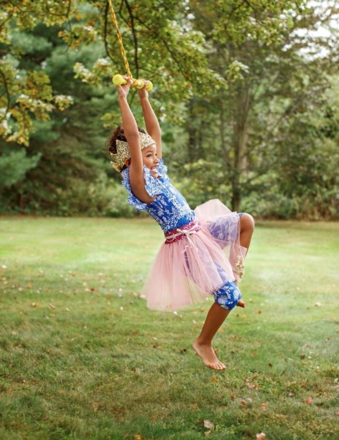 girl dressed in a princess dress with crown outdoor activities for kids swinging on a rope hanging from a tree