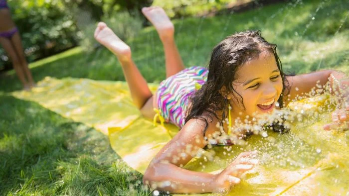 girl going down a water slide backyard games for kids plastic cloth placed on the grass