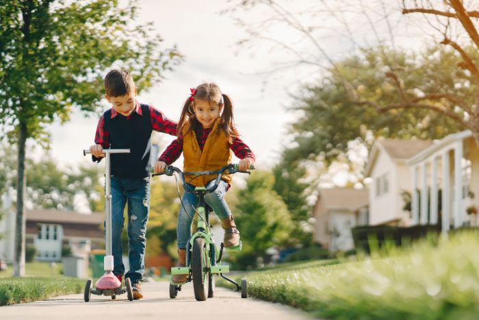 girl riding a bike outdoor activities for toddlers boy next to her riding on a scooter on the sidewalk