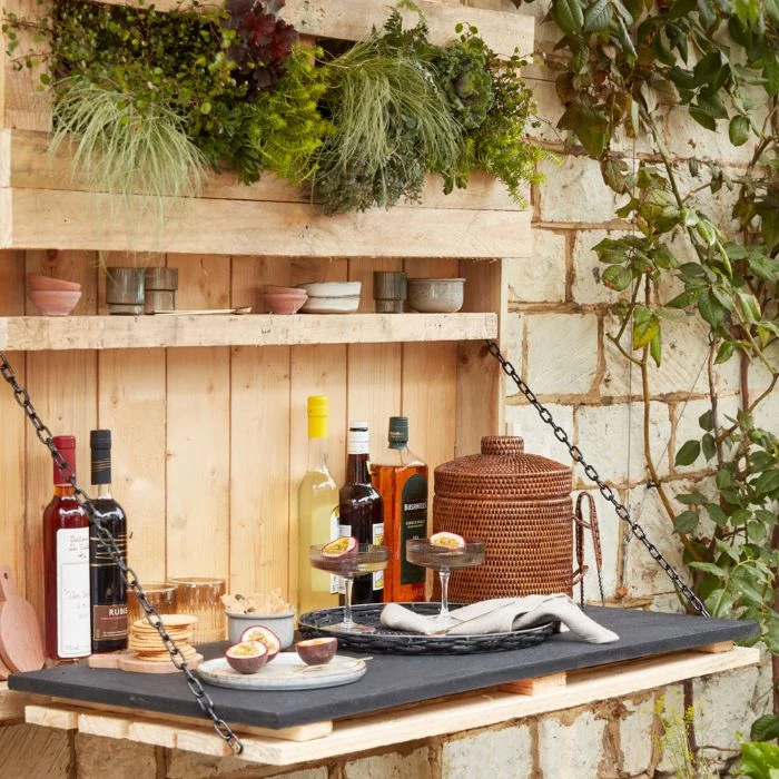 hanging wooden bar with plants backyard tiki bar different bottles and cocktail glasses on it