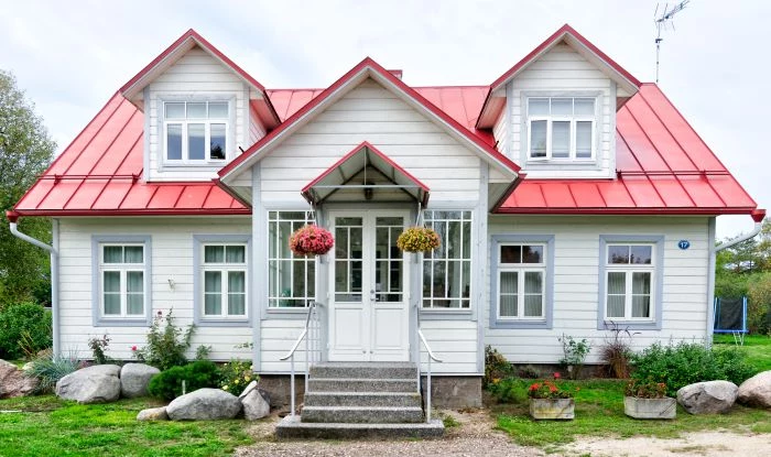 house with white siding red roof door installation large boulders in front with flower beds