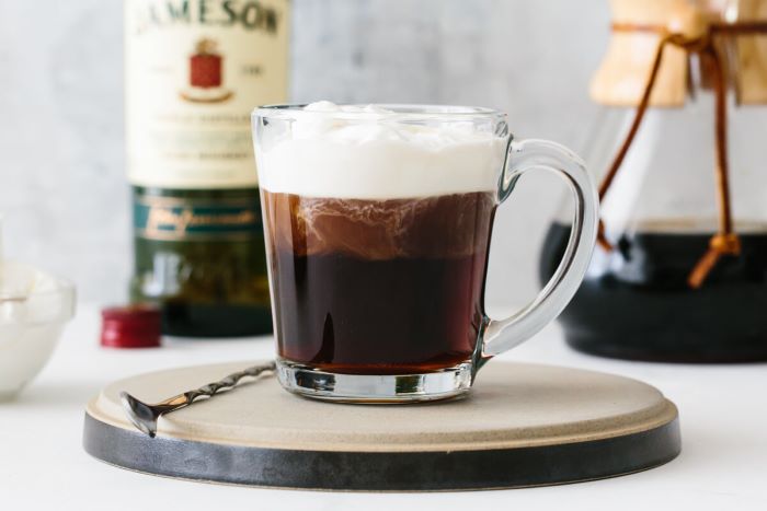 irish coffee with whipped cream on top poured in glass mug cold brew coffee spoon on the side