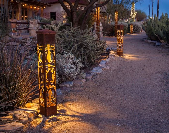 lanterns with different height and decorations placed along a pathway string light pole next to flower beds