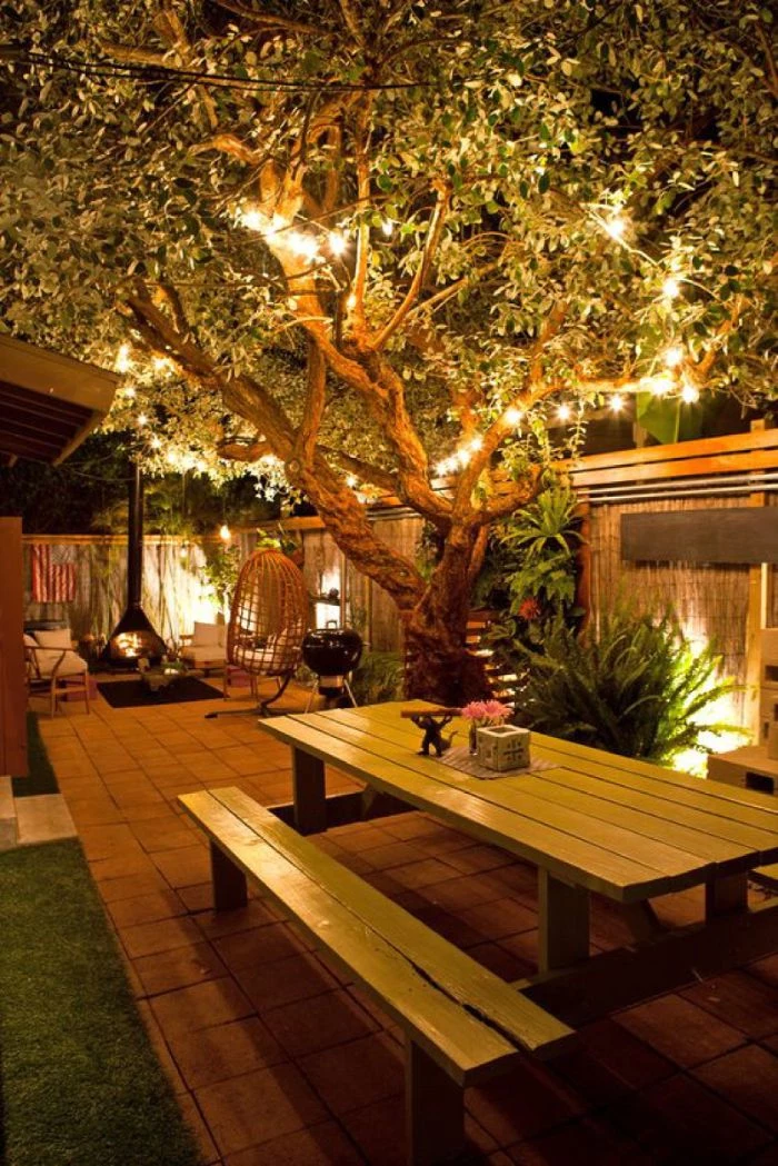 large tree wrapped with strings of lights outdoor lighting ideas wooden bench and table underneath