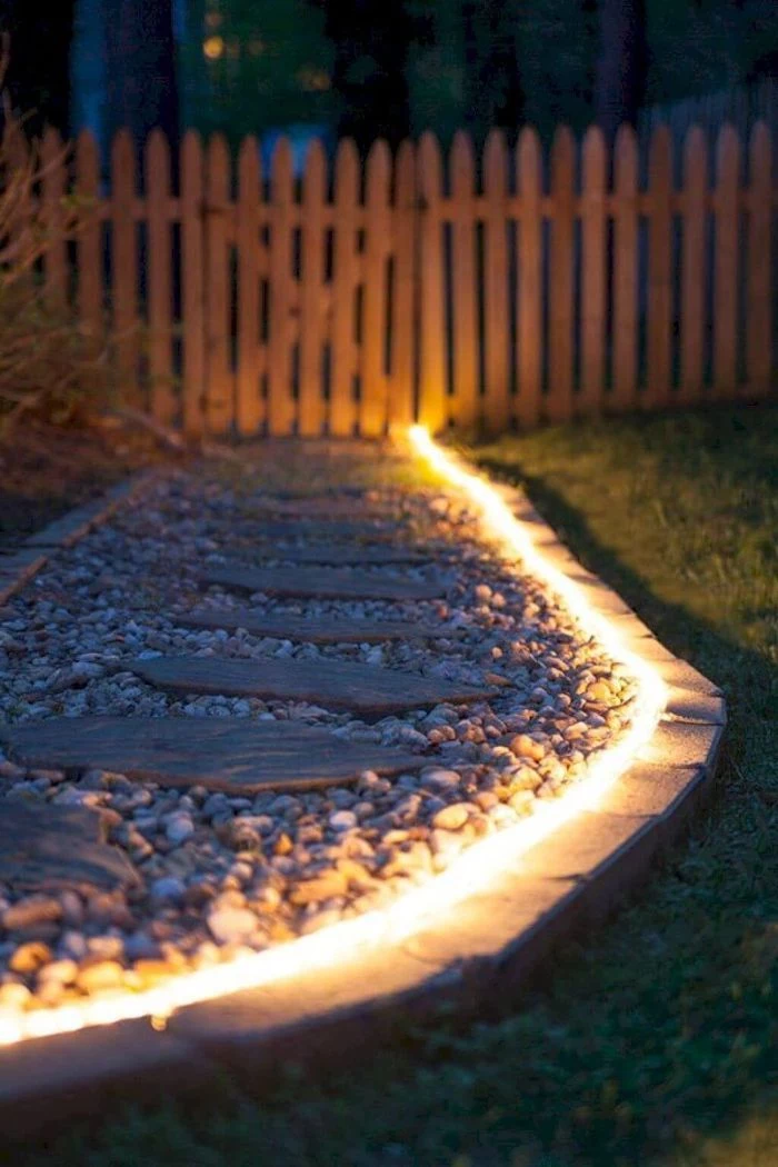 led lights hose placed along a pathway made with gravel and stones backyard lighting ideas wooden fence