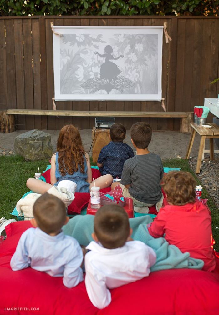 lots of kids sitting on red throw pillows with pop corn and soda fun games to play outside watching a film