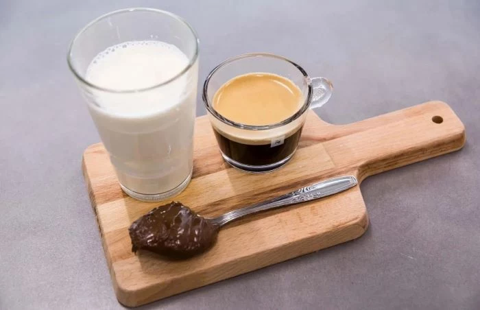 milk espresso in two separate glasses spoonful of hazelnut spread how to make iced coffee at home placed on wooden board
