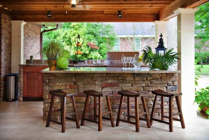 outdoor kitchen island made with stones outdoor patio bar black stoold in front of it wooden enclosure