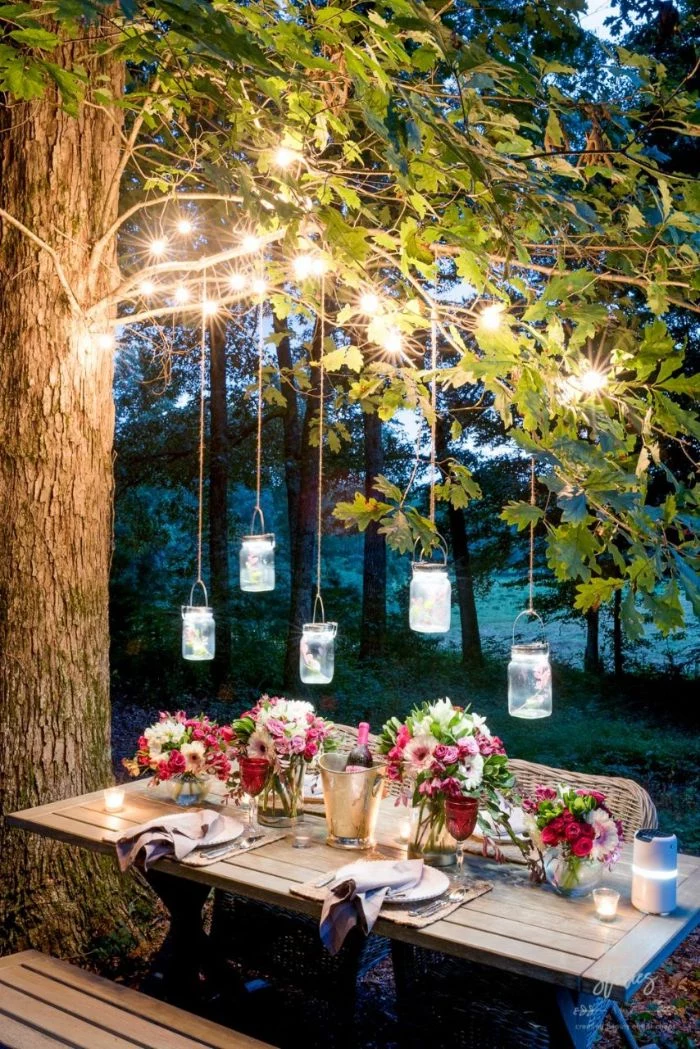 outdoor string lights wooden table and bench placed under a tree mason jars and string lights hanging above it