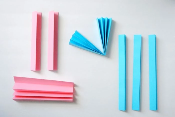pink and blue paper folded as an acordeon placed on white surface baby shower centerpiece ideas step by step diy tutorial