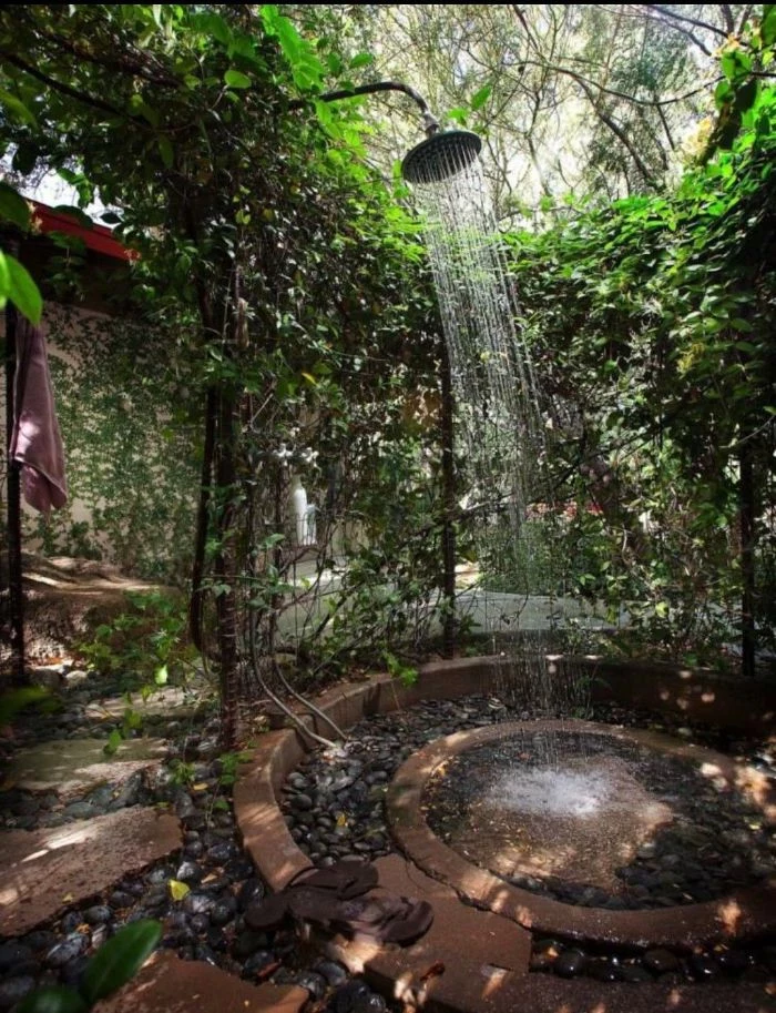 rocks and tiles on the floor freestanding outdoor shower surrounded by plants and greenery