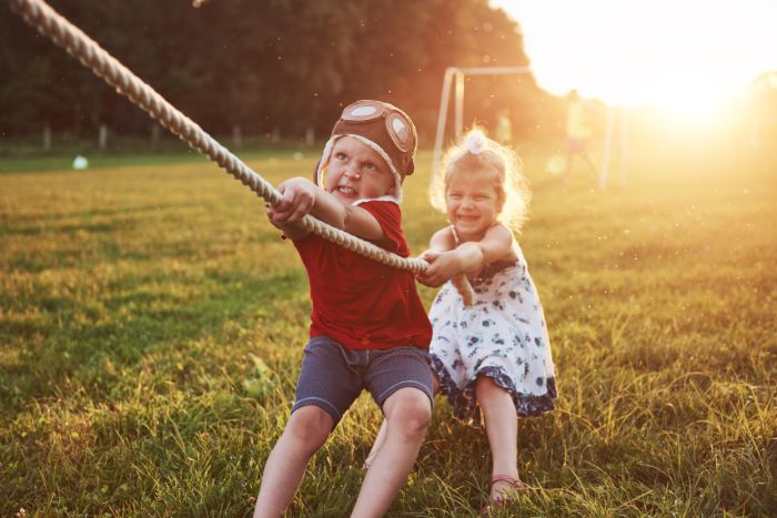 things to do outside boy girl pulling rope playing tug of war in the park sun shining above them